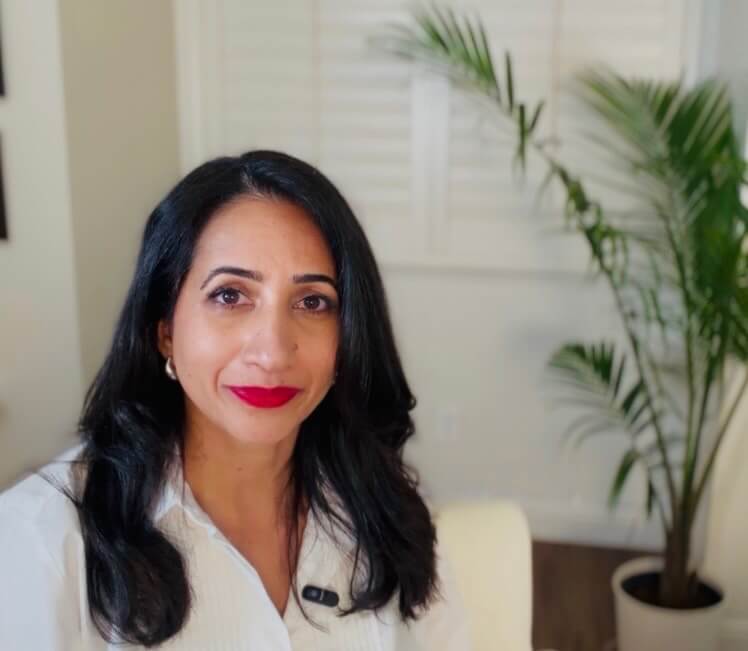 Aman Gohal, professional consultant, seated indoors wearing a white blouse in a modern office setting